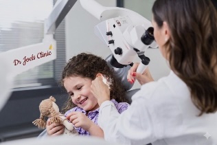 Happy child playing with toy while undergoing microscopic wax removal